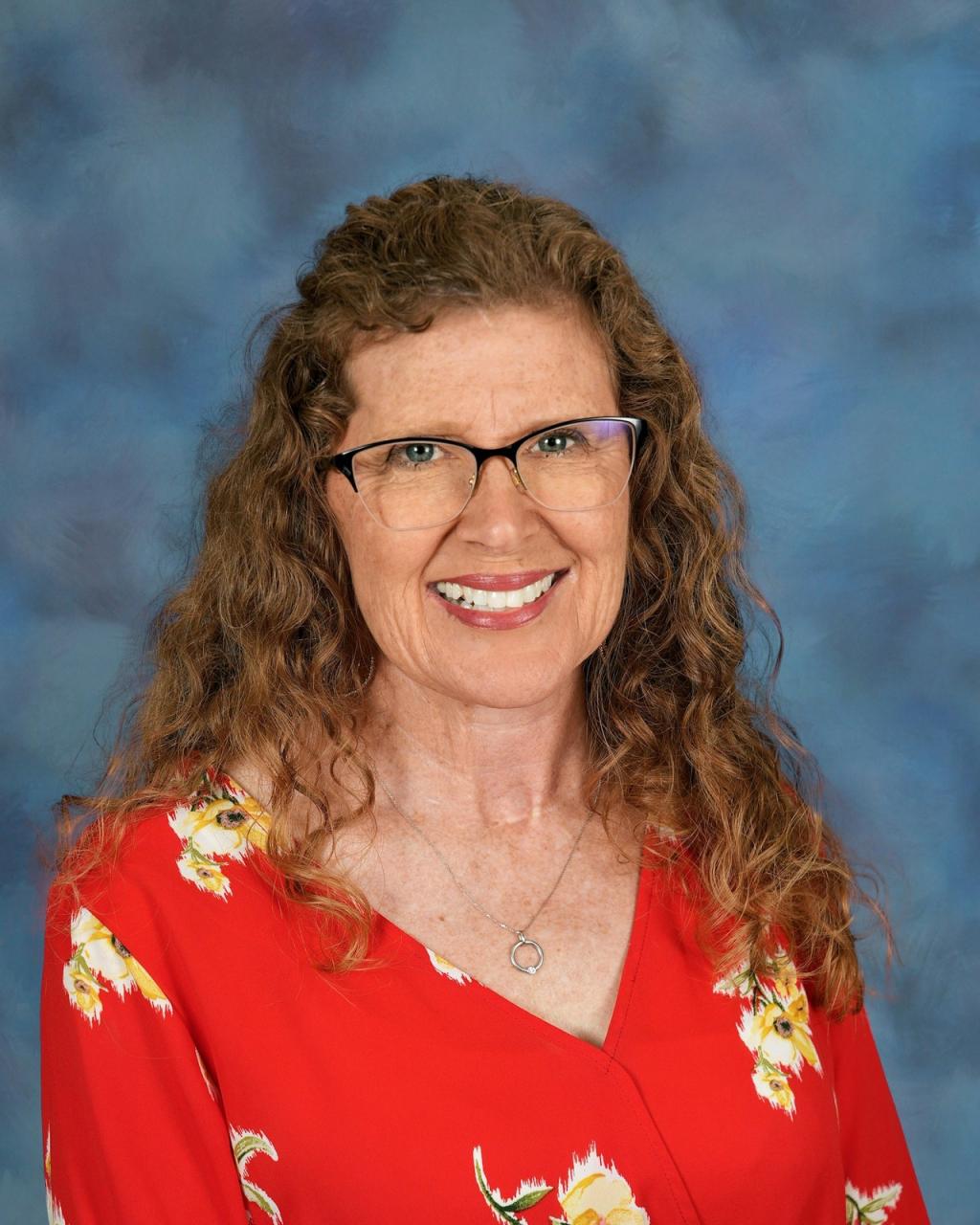 Lady with red hair, wearing glasses and a red top with flowers